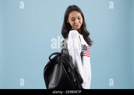 Jeune femme souriante tenant un sac à dos noir regardant par-dessus l'épaule Banque D'Images