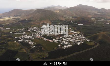 Paysage aérien d'un village blanc à Lanzarote entouré de champs volcaniques et de vignobles, avec des parcelles viticoles et lumière magique sur h accidenté Banque D'Images