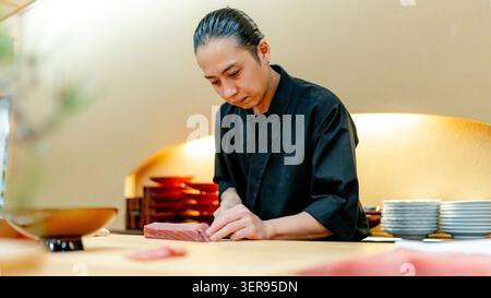 Un chef de sushis expérimenté tranche du thon rouge Miyagi Pacific dans un restaurant japonais de Tokyo, préparant avec précision des sashimi maguro de qualité supérieure. Banque D'Images