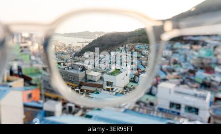 Vue panoramique du village culturel Gamcheon à Busan, Corée du Sud, capturée à travers une paire de lunettes. Les maisons vibrantes et le paysage vallonné créent une photo Banque D'Images