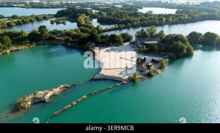Vue aérienne d'une gravière active extrayant des agrégats, créant des lacs turquoise. Machines industrielles, bancs sablonneux et tuyaux présents Banque D'Images