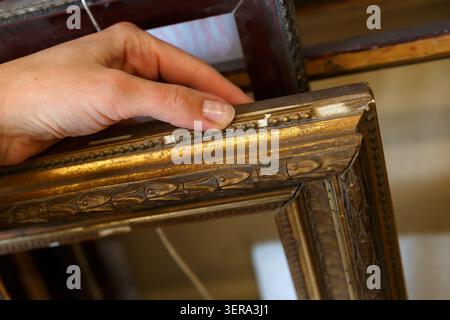 Une personne tient un cadre vintage soigneusement dans un magasin d'art situé au centre-ville. La boutique est bien éclairée et dispose de différents cadres. Banque D'Images
