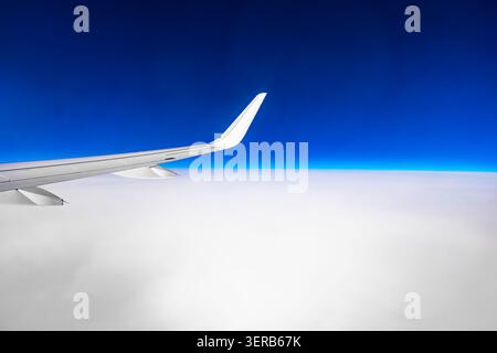 Vue depuis la fenêtre de l'avion montrant l'aile de l'avion volant haut au-dessus d'épais nuages blancs sous le ciel bleu profond de l'horizon Banque D'Images