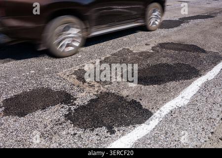 Voiture conduisant sur une route avec plusieurs plaques d'asphalte après réparation de nids de poule. Concept de mauvaises conditions routières, asphalte usé, dommages au véhicule, suspension et Banque D'Images