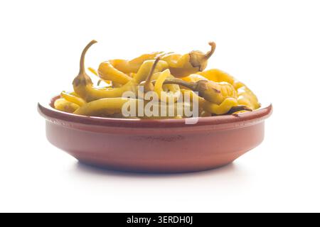 Poivrons de banane marinés acidulés empilés dans un bol en céramique rustique sur un fond blanc, présentant une couleur jaune vif, une texture brillante et une collation zestée ou Banque D'Images