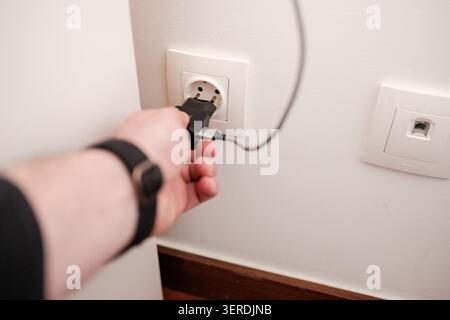 Main branchement d'un chargeur à une prise murale blanche pour l'alimentation Banque D'Images