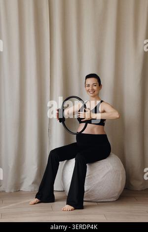 Femme enceinte assise sur le ballon de fitness tenant l'anneau de pilates pendant l'entraînement prénatal Banque D'Images