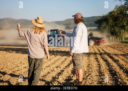 Travail d'équipe agricole. Agriculteur et agronome cherchent à semer des cultures par tracteur dans les champs cultivés à la ferme Banque D'Images