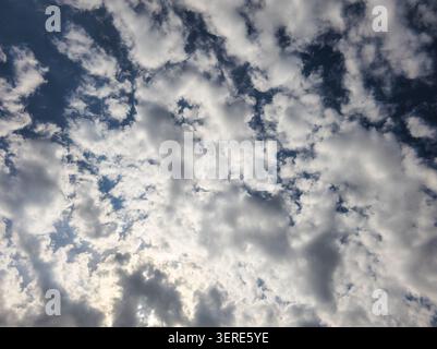 Vaste étendue de ciel remplie de nuages blancs et gris sur bleu profond. La lumière du soleil filtre à travers, créant des ombres et des lumières spectaculaires. Banque D'Images