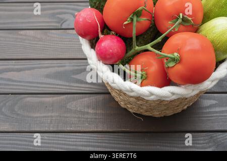 Légumes frais dans un panier en osier avec tomates, concombres, radis, courgettes et aneth sur fond de bois. Banque D'Images