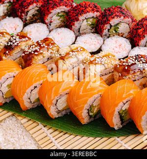 Des rouleaux de sushi colorés sont disposés soigneusement sur un tapis de bambou. Différents types de saumon sont composés de saumon frais, de légumes croquants et de sauces savoureuses. Parfait pour un repas décontracté ou une réunion. Banque D'Images