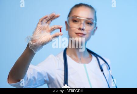 Femme médecin ou scientifique dans une blouse de laboratoire et stéthoscope tenant une pilule rouge unique, symbolisant le traitement médical et l'innovation Banque D'Images