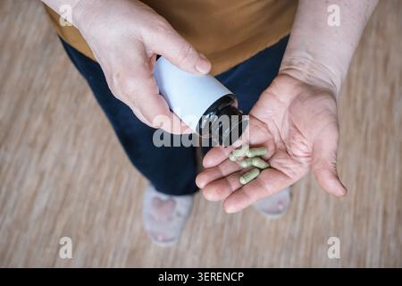 Femme âgée distribuant des capsules vertes de la bouteille dans sa main pour la santé Banque D'Images