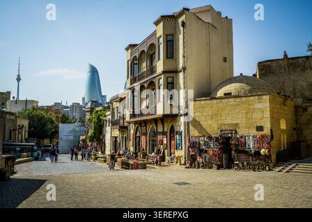 Cette scène de rue animée capture une journée ensoleillée dans la vieille ville historique de Bakou, Icherisheher, avec des bâtiments traditionnels et des étals de marché chargés de SO Banque D'Images