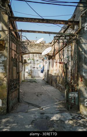 Cette image capture une entrée de ruelle étroite et altérée dans un ancien quartier résidentiel de Bakou, Azerbaïdjan, montrant des murs en ruine, gat de métal rouillé Banque D'Images