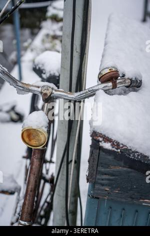 Une vue rapprochée du guidon, de la cloche et du phare d'un vieux vélo rouillé, le tout lourdement chargé de neige blanche et fraîche. La scène capture un calme, froid Banque D'Images