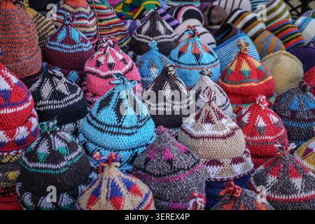 Un gros plan capture une multitude de chapeaux tricotés marocains traditionnels, empilés haut et remplissant le cadre d'une riche tapisserie de couleurs et de géometr Banque D'Images
