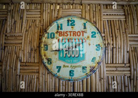 Vue rapprochée d'une horloge vintage rustique et vieillie avec texte « BISTROT » et « GOOD FOOD » avec des icônes de couverts. Le timepie circulaire de couleur crème Banque D'Images