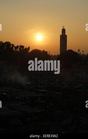 Le minaret de la Koutoubia se dresse comme une silhouette proéminente contre un ciel chaud et doré de coucher de soleil, dominant la place historique Jemaa el-Fnaa à Marrakech, Banque D'Images