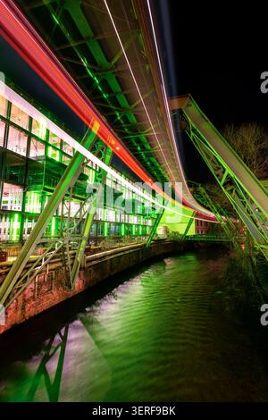 Photo de nuit de l'unique chemin de fer suspendu de Wuppertal (Allemagne) avec le système historique de rails verts au-dessus de la rivière Wupper dans le centre-ville d'Elberfeld Banque D'Images
