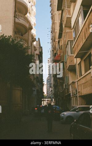 Une rue latérale étroite et profondément ombragée à Alexandrie, en Égypte, photographiée regardant vers une ouverture lumineuse où la ruelle rencontre un boulevard plus large. Orna Banque D'Images