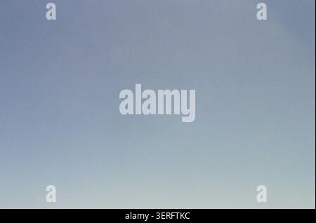 Un ciel minimaliste et sans nuages capturé avec un dégradé bleu-gris doux passant des teintes plus profondes en haut aux tons plus pâles en bas. La texture du grain du film ajoute un Banque D'Images
