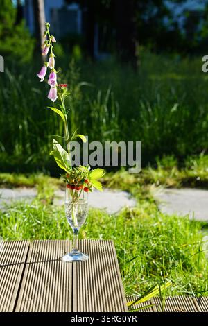 Un vase en verre avec un bouquet sauvage de digitales et de fraises sur une table de jardin Banque D'Images