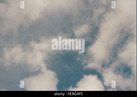 Ciel couvert Moody rempli de nuages blancs et gris qui se séparent pour révéler des taches de ciel bleu sarcelle profond, capturées avec une esthétique de film vintage Banque D'Images