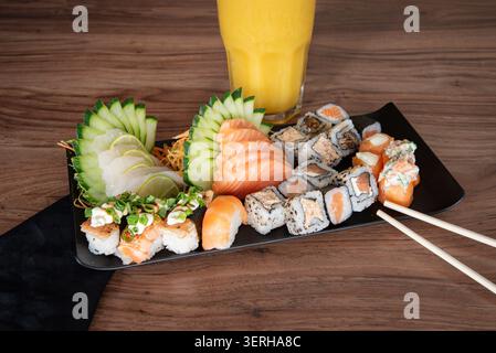 Assortiment de sushi, maki et sashimi servi sur assiette foncée avec jus d'orange. Fond en bois, lumière douce de studio. Concept alimentaire pour une alimentation saine, Banque D'Images