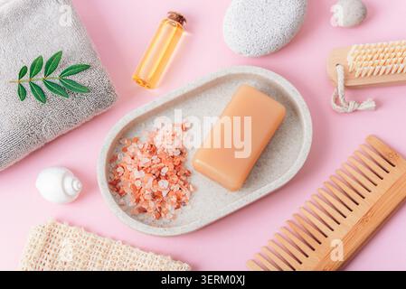 Accessoires de spa avec savon, sel de bain, huile essentielle, serviette et peigne en bois sur fond rose. Vue de dessus, pose à plat Banque D'Images