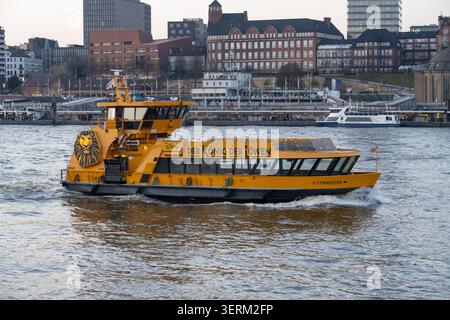 Hambourg, Allemagne - 28 février 25 : ferry de passagers jaune sur l'Elbe dans le port de Hambourg avec le front de mer de la ville en arrière-plan, Allemagne. Banque D'Images