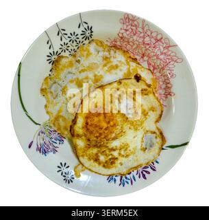 Gros plan de deux œufs frits servis sur une assiette florale décorative placée sur fond blanc, mettant en valeur un petit déjeuner fait maison avec des bords dorés et doux Banque D'Images