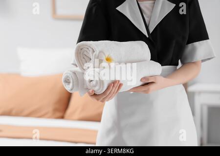 Femme de chambre avec des serviettes propres et fleur de plumeria dans la chambre d'hôtel Banque D'Images