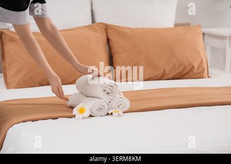 Femme de chambre avec pile de serviettes propres et fleurs de plumeria sur le lit dans la chambre d'hôtel Banque D'Images