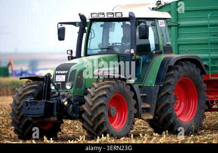 Un tracteur Fendt Favorit 716 vert moderne doté de roues rouges distinctives tire une grande remorque sur un champ récolté pendant la récolte d'automne. Banque D'Images