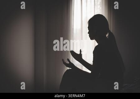 Silhouette féminine dans la prière avec les mains levées dans le culte, représentant la foi chrétienne, la spiritualité, la confiance et la réflexion personnelle dans un atmos serein Banque D'Images