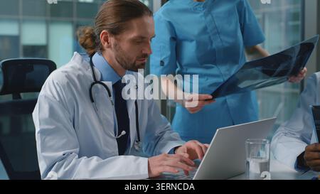 L'équipe médicale multiraciale de médecins discutant des radiographies travaillant avec un ordinateur portable parlant à la conférence de médecine. Trois chirurgiens praticiens Banque D'Images