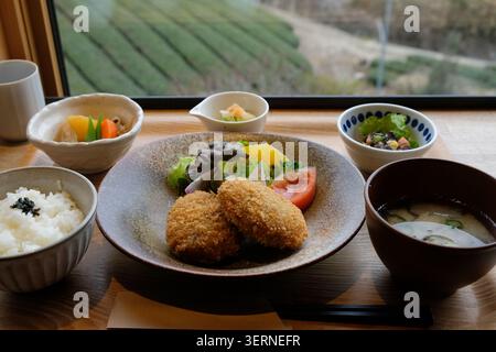 Service de repas japonais avec croquettes, riz, soupe miso et accompagnements près d'une fenêtre donnant sur les champs de thé vert, Wazuka Banque D'Images