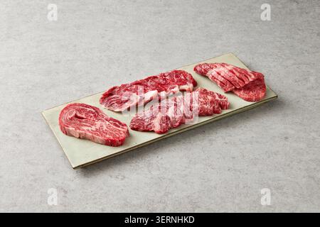 Coupes de bœuf et de porc crues fraîches coréennes affichées sur un tableau d'ardoise noire avec de l'ail, du romarin et de l'assaisonnement sur un fond sombre Banque D'Images