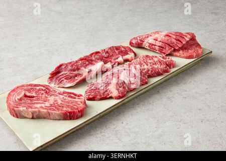 Coupes de bœuf et de porc crues fraîches coréennes affichées sur un tableau d'ardoise noire avec de l'ail, du romarin et de l'assaisonnement sur un fond sombre Banque D'Images