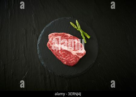 Coupes de bœuf et de porc crues fraîches coréennes affichées sur un tableau d'ardoise noire avec de l'ail, du romarin et de l'assaisonnement sur un fond sombre Banque D'Images