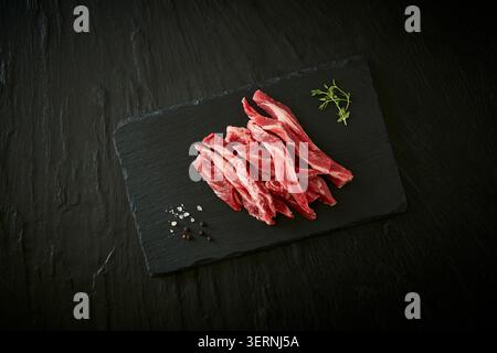 Coupes de bœuf et de porc crues fraîches coréennes affichées sur un tableau d'ardoise noire avec de l'ail, du romarin et de l'assaisonnement sur un fond sombre Banque D'Images