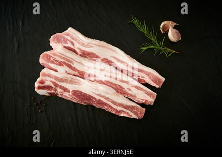 Coupes de bœuf et de porc crues fraîches coréennes affichées sur un tableau d'ardoise noire avec de l'ail, du romarin et de l'assaisonnement sur un fond sombre Banque D'Images