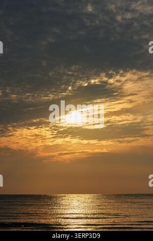 Paysage serein Golden Hour avec un soleil brillant qui brille à travers les nuages et se reflète sur les vagues douces de l'océan montrant la nature paisible Banque D'Images