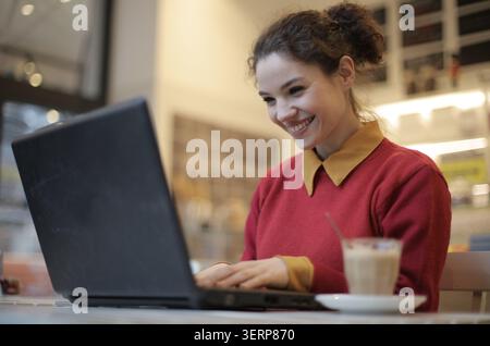 Heureuse jeune femme travaillant sur ordinateur portable au café Banque D'Images