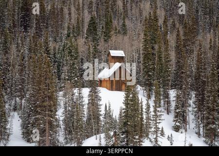 Vue aérienne d'une structure minière historique en bois entourée d'arbres à feuilles persistantes recouverts de neige dans une forêt dense à Ouray, Colorado, États-Unis. Banque D'Images