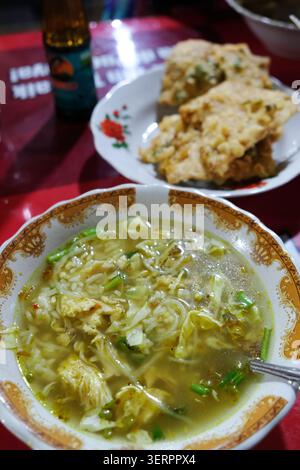 Soupe de poulet indonésienne traditionnelle ou ayam soto servi avec du riz et un côté de tempeh frit croustillant pour le petit déjeuner dans un restaurant local à Yogyakarta Banque D'Images