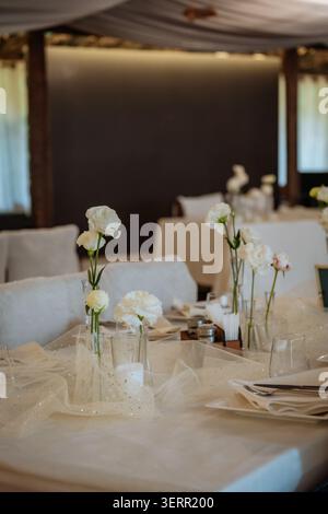 Arrangement sophistiqué de table de mariage avec fleurs blanches fraîches dans des vases en verre clair, bougies brillantes, tulle étincelant délicat et tablewa fin Banque D'Images