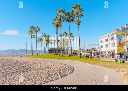 Venice Beach, Californie - 8 janvier 2026 : sentier pavé de promenade à Venice Beach, Californie, avec de grands palmiers, plage de sable, bâtiment côtier Banque D'Images