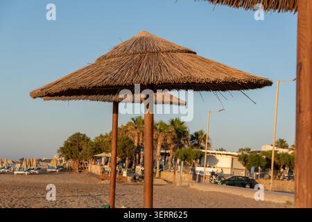 Une belle vue sur les parasols de chaume naturels sur une plage de sable vide pendant la lumière chaude de l'après-midi. Le paysage côtier dispose d'une promenade de villégiature Wit Banque D'Images